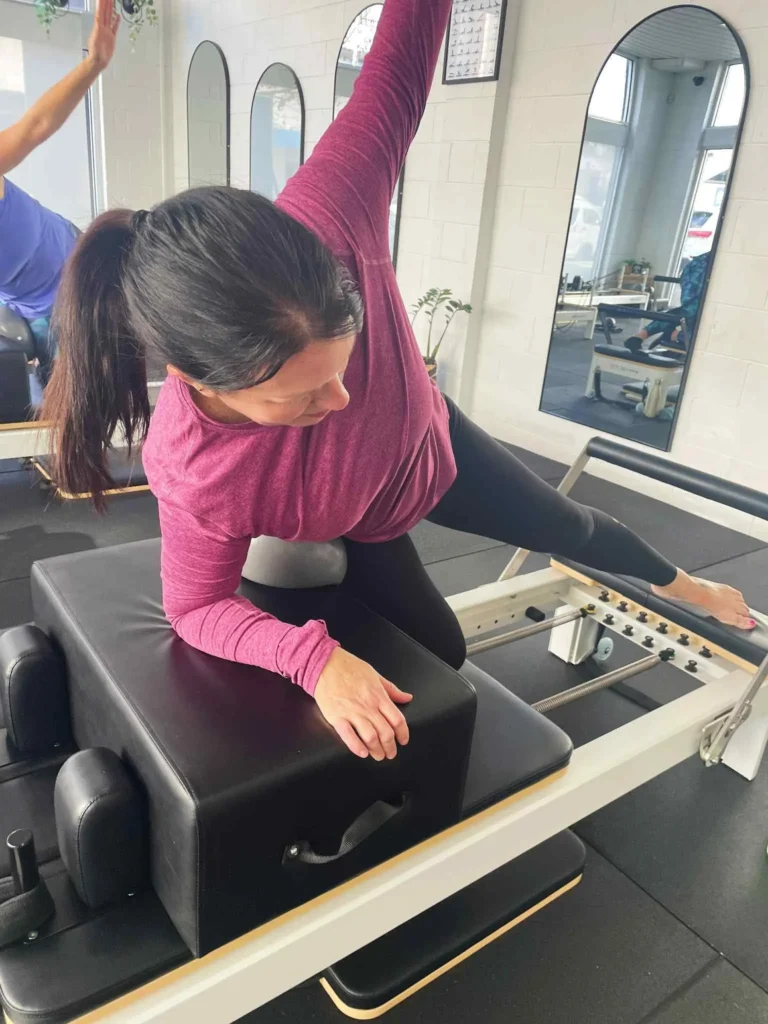 Woman performing a side bend on a Pilates reformer to strengthen the obliques and improve mobility.
