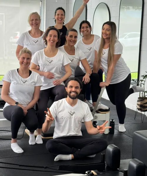 4You Pilates team group photo in the studio, smiling in front of reformer equipment.